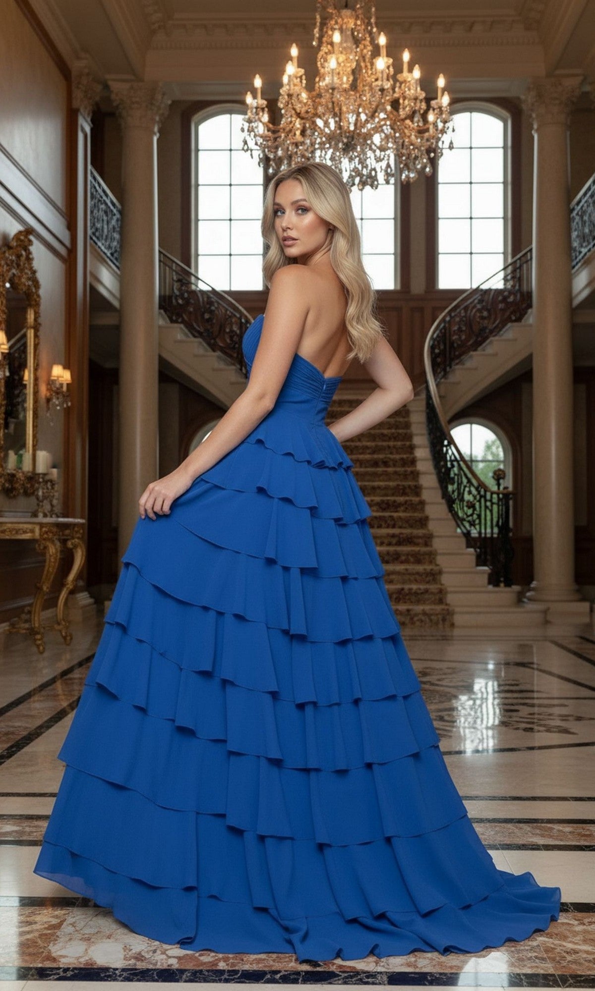 Wearing the Long Prom Dress: Poly USA 25012—with a strapless chiffon design, sweetheart neckline, and tiered A-line skirt—a woman stands in an elegant marble-floored foyer with a chandelier and staircase.